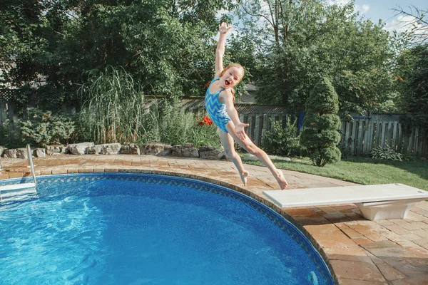 Girl child diving jumping  in water on home backyard pool. Funny cute kid enjoying and having fun in swimming pool on summer day. Summer outdoor water activity for kids.