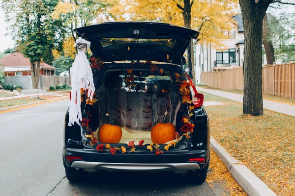 Trick or trunk. Black car trunk decorated for Halloween. Autumn fall decor with red pumpkins and yellow leaves for traditional October holiday outdoor. Social distance during coronavirus covid-19.