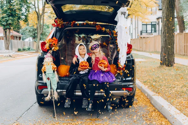 Trick or trunk. Children celebrating Halloween in trunk of car. Boy and girl with red pumpkins celebrating traditional October holiday outdoor. Social distance and safe alternative celebration.