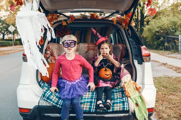 Trick or trunk. Children siblings sisters celebrating Halloween in trunk of car. Friends kids girls preparing for October holiday outdoor. Social distance and safe alternative celebration.