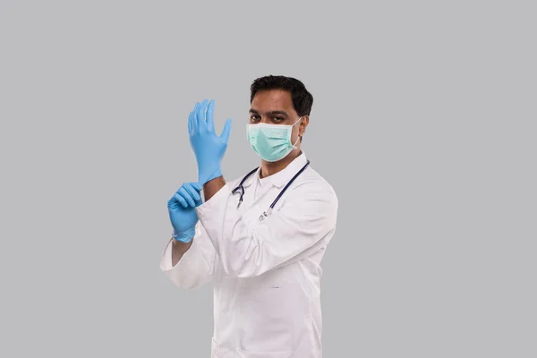 Doctor se pone guantes y usa máscara médica aislada. Hombre indio Máscara de protección médica Ropa de trabajo. Concepto médico Virus Corona . — Foto de Stock