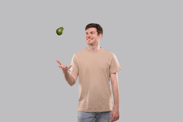 Een glimlachende man die Avocado geïsoleerd gooit. Een man die Avocado vangt. Gezond voedselconcept — Stockfoto