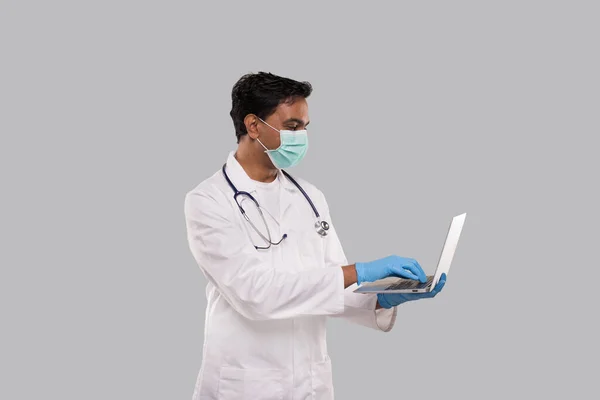 Medico Utilizzando Laptop Indossare Maschera Medica e Guanti Isolati. Maschio medico indiano con computer portatile in mano . — Foto Stock