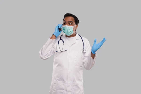 Läkare pratar på telefon upphetsad, bär medicinsk mask och handskar. Indiska man läkare med telefon isolerad — Stockfoto
