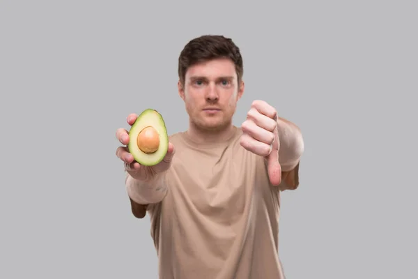 Hombre mostrando aguacate y pulgar hacia abajo de cerca aislado. Aguacate cortado por la mitad. No Aguacate, Detener el concepto de aguacate — Foto de Stock