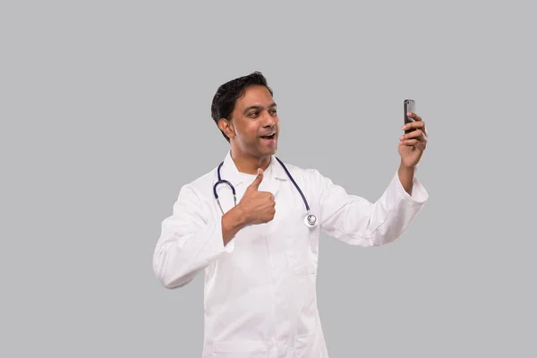 Dottore avendo videochiamata sul telefono mostrando pollice su isolato. La videochiamata di Indian Man Doctor. Medicina online. Medico utilizzando il telefono . — Foto Stock