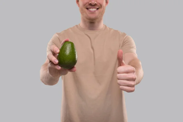 Man toont Avocado en duim van dichtbij geïsoleerd. Gezond leven, eet groen concept — Stockfoto