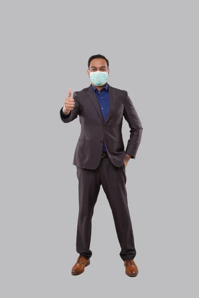 Affärsman bär medicinsk mask Visar tumme upp Isolerad. Indiska affärsman stående full längd — Stockfoto