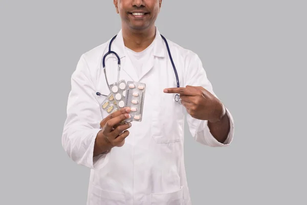 Человек-доктор указывает на таблетки крупным планом. Доктор держит таблетки. Индийский доктор изолирован . — стоковое фото