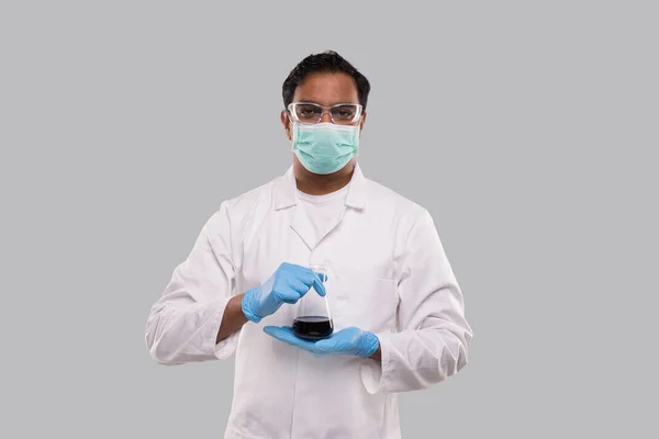 Männlicher Arzt hält Kolben mit farbenfroher Flüssigkeit und trägt medizinische Maske, Handschuhe und Brille isoliert. Wissenschaft, Medizin, Viruskonzept. Indischer Mann Arzt lächelnd. — Stockfoto