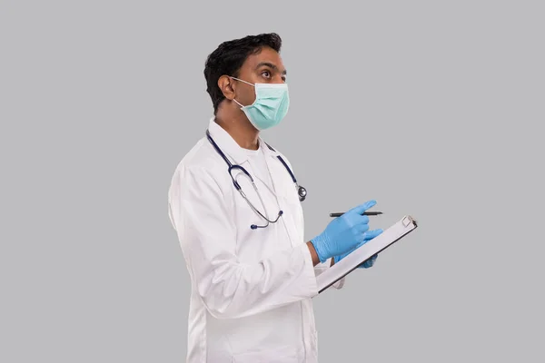 Doctor Writing Down Good Idea in Klembord Het dragen van medische maskers en handschoenen. Indian Man Doctor klembord geïsoleerd — Stockfoto