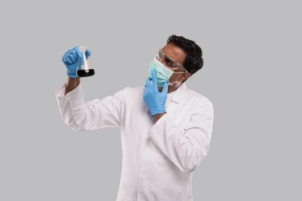 Maschio medico esame Flask con Colorfull liquido indossare maschera medica, guanti e occhiali isolati. Scienza, Medicina, Concetto Virus. Indiano uomo dottore sorridente . — Foto Stock