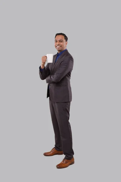 Podnikatel stojící a držící šálek kávy. Indický podnikatel stojící plnou délku v obleku s kávovým pohárem — Stock fotografie