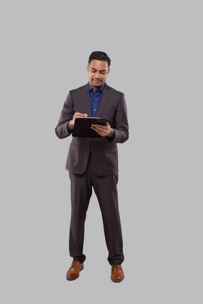 Biznesmen piszący w izolatce. Indian Business man Standing Full Length z klapką w dłoniach — Zdjęcie stockowe