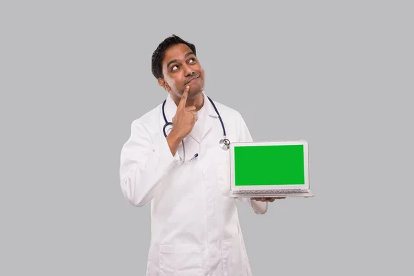 Arzt zeigt Laptop auf grünem Bildschirm und denkt isoliert nach oben. Indischer Arzt mit Laptop in der Hand. Konzept der Online-Medizin — Stockfoto