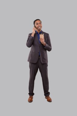 İş adamı telefonda kahve içip kupayı izole etmek için konuşuyor. Elinde kahve kupası olan Hintli bir işadamı ayakta duruyor. Erkek