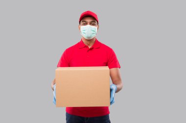 Ellerinde tıbbi maske ve eldivenler olan teslimatçı kutusunu izole etti. Kırmızı Tişörtlü Kızılderili Teslimatçı Çocuk Tarafından İzleniyor. Eve Teslimat. Karantina Kahramanı. Kargo