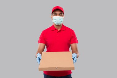 Teslimatçı Pizza Kutusu Ellerinde Tıbbi maske ve eldivenler ile izole edildi. Kırmızı Tişörtlü Kızılderili Teslimatçı Çocuk. Kargo