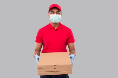 Teslimatçı Üç Pizza Kutusu Ellerinde Tıbbi maske ve eldivenler var. Kırmızı Tişörtlü Kızılderili Teslimatçı Çocuk. Yemek Teslimatı