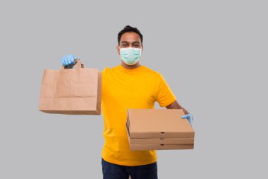 Karton Torbalı Teslimatçı ve Ellerinde Tıbbi Maske ve Eldiven Giyen Üç Pizza Kutusu İzole Edildi. Sarı üniformalı Kızılderili Teslimatçı Çocuk. Ev yemeği teslimatı. Kağıt Torba