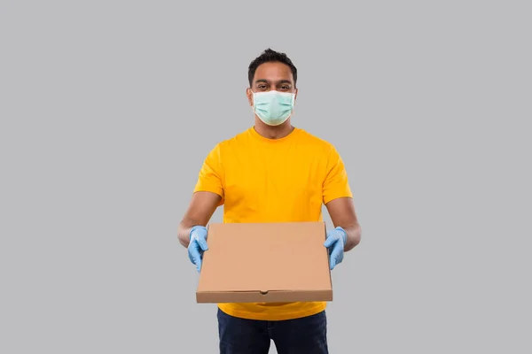 Entrega hombre caja de pizza en las manos que lleva máscara médica y guantes aislados. Camiseta amarilla Indian Delivery Boy. Hombre con pizza en las manos — Foto de Stock