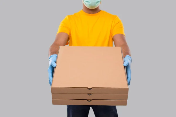 デリバリーマン医療マスクと手袋を着用して手に3つのピザボックスが隔離されました。黄色のTシャツインド配信少年。ピザを手にした男 — ストック写真
