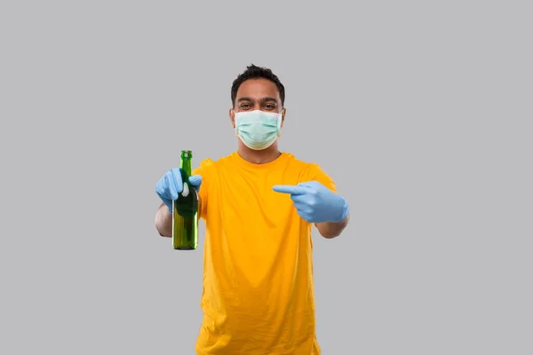Indischer Mann zeigt auf Bierflasche mit medizinischer Maske und Handschuhen. — Stockfoto