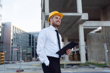 Hardhat Holding Pano 'sunu elinde tutan bir iş adamı. İnşaat Kontrol Merkezi Binası. İnşaat İşleri 'nin yanında Gülümseyen Adam