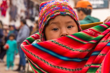 Chinchero, Peru - Ekim 05, 2018: Geleneksel renkli giysiler giymiş yerli kadın bebeği sırtında olarak yerel markette yürüyor