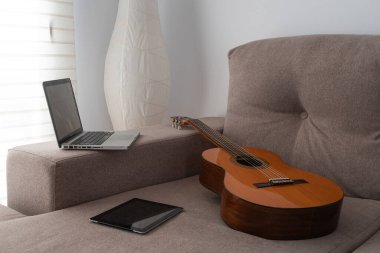 İspanyol gitarı, dizüstü bilgisayar ve tablet oturma odasındaki koltukta..