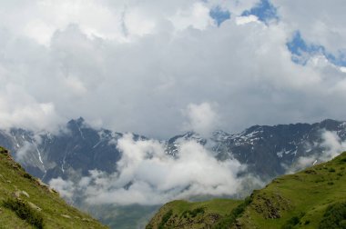 Güneş ışığı görkemli dumanlı bulutların arasından karlı dağların üzerinde süzülüyor. Açık yeşillik tepesinden kayalarla manzarayı seyret. Yeşil tepeler derin sis duvar kağıdıyla tıka basa doludur.