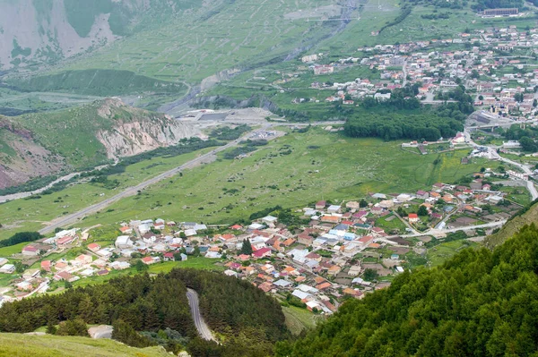 A small town in the gorge with large green forest and mountains landscape. Top view on the roadway between the pine forest in hills leading to little houses. Countryside healthy living concept