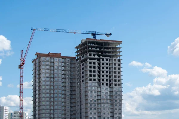 Building under construction against blue sky with clouds. Tower crane lifting cement bucket during construction a multi-storey residential building. Concrete interior of unfinished cityscape house.