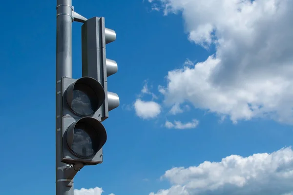 Switched off grey traffic light against bright blue cloudy sky background with copy space. Offline streetlight signal in the city crossroad. Urban traffic system problems due to deactivate semaphore.