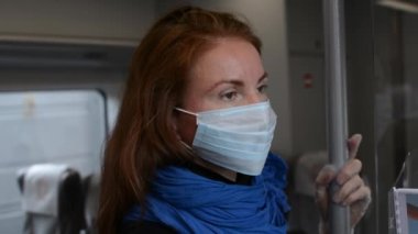 Tek kullanımlık maske takan Avrupalı bir kızıl kızın portresi toplu taşıma aracında kameraya doğru dönüyor. Yakın görüş. Covid salgını ve kendini izole etme kısıtlamaları sırasında tıbbi maske takan bayan yolcu..