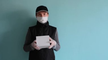 Siyah üniformalı, koruyucu tıbbi maskeli ve tek kullanımlık eldivenli kadın kurye logoti veya ünvan için yeri olan beyaz bir kutu taşıyor. Covid-19 virüs salgını sırasında teslimat hizmeti