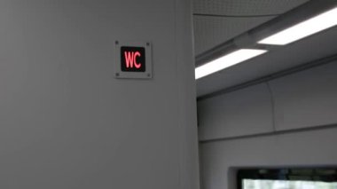 Tren hareket ederken yolcu vagonunda kırmızı ile parlayan WC yazıtları. Şehrin gri iç kısımlarında tuvalet ışığı. Ekspres trende ışıklar ve titreşen nesneler var. Boşluğu kopyala.