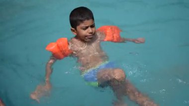 Havuzda yüzen mutlu Hintli çocuk, sıcak yaz tatillerinde hava tüpüyle birlikte yüzen çocuk, büyük bir havuzda yüzen çocuk..