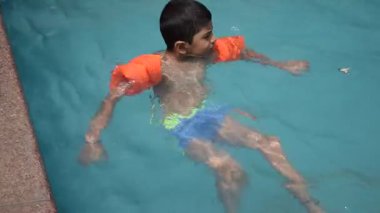 Havuzda yüzen mutlu Hintli çocuk, sıcak yaz tatillerinde hava tüpüyle birlikte yüzen çocuk, büyük bir havuzda yüzen çocuk..