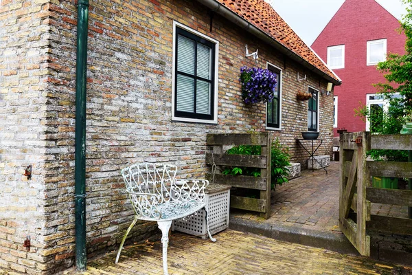 オランダ ヒンデロープンレンガ造りの家の前に白い東洋のベンチとロマンチックな座っています 紫色の花で飾られた家に木製の門を開きます — ストック写真