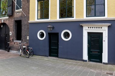 Hollanda Dordrecht caddesi, mor sarı duvarlı renkli ev, beyaz kapılı ön kapı ve yuvarlak pencereler. Evin önünde 2 eğilmiş tekerlek var..