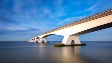 Zeeland Köprüsü - nehrin üzerindeki uzun beyaz köprü, dinamik bulutlu güzel mavi gökyüzü. Uzun zamandır, Oosterschelde 'nin sakin suyu ..