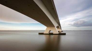 Zeeland Köprüsü - nehrin üzerindeki uzun beyaz köprü, dinamik bulutlu güzel mavi gökyüzü. Uzun zamandır, Oosterschelde 'nin sakin suyu ..