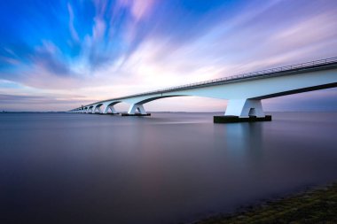 Zeeland Köprüsü - nehrin üzerindeki uzun beyaz köprü, dinamik bulutlu güzel mavi gökyüzü. Uzun zamandır, Oosterschelde 'nin sakin suyu ..