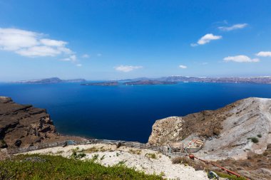 Santorini, Caldera, Caldera 'nın kayalık kıyı şeridi ve arka plandaki iki volkanik ada. Tepenin aşağısında yeni bir ev. Güzel açık mavi gökyüzü.