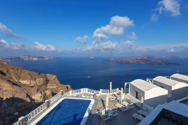 Santorini, uçurumdan aşağıya, güzel havuza ve beyaz evlere kadar uzanan kalderanın manzarası. Arka planda adacıklar ve güzel mavi deniz.