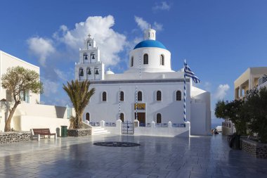 Santorini, Oia - Beyaz çan kulesinin manzarası, arka planda mavi kubbeli bir kilise.