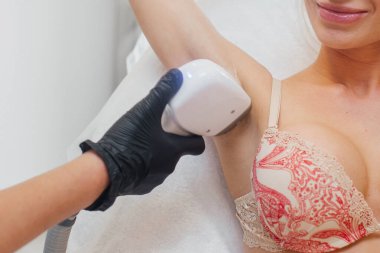 Doktor kızın koltuk altının epilasyonunu yapıyor. Lazerle saç aldıran bir kadın. Kozmetik salonunda lazer tedavisi. Koltuk altı lazer epilasyonu olan bir kadın. Vücut Bakımı.