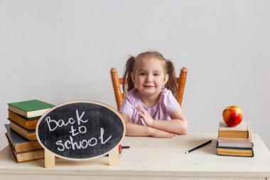 Okuldaki küçük tatlı kız ders kitaplarıyla masasında oturuyor. Çocuk derste öğreniyor. Okula geri dön..