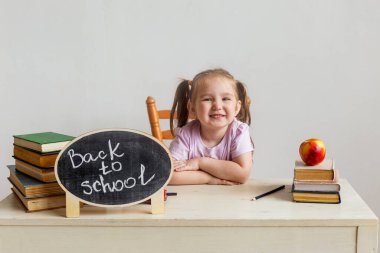 Okuldaki küçük tatlı kız ders kitaplarıyla masasında oturuyor. Çocuk derste öğreniyor. Okula geri dön..